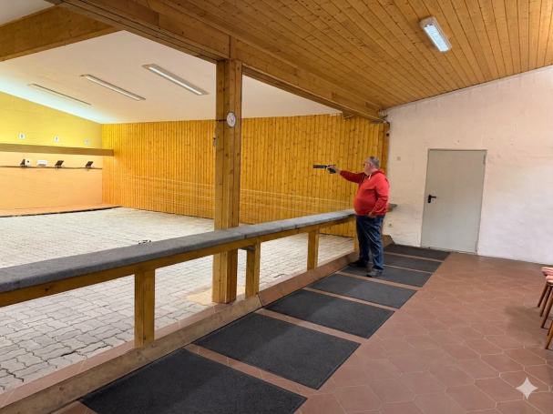 Mann zielt mit einer Pistole auf eine Zielscheibe in einer Schießhalle.